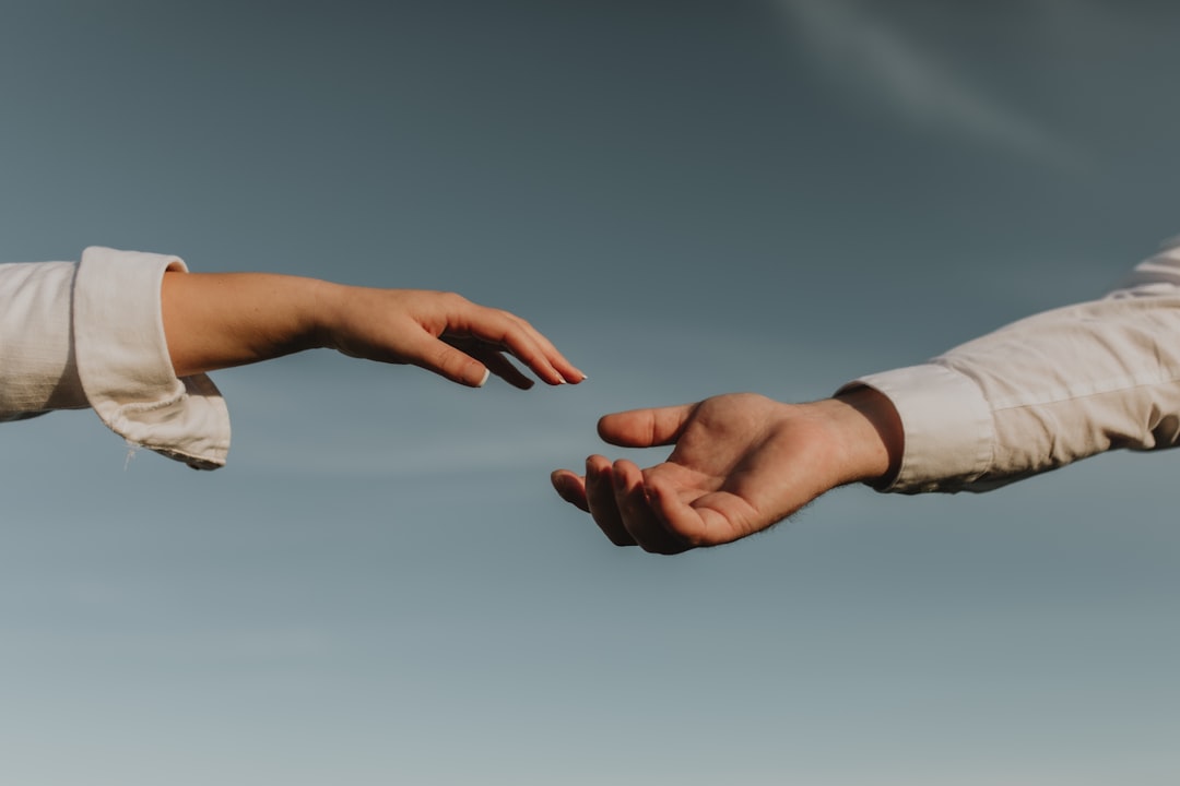 veteran service dog grants — Two hands in white sleeves reaching toward each other against a clear blue sky